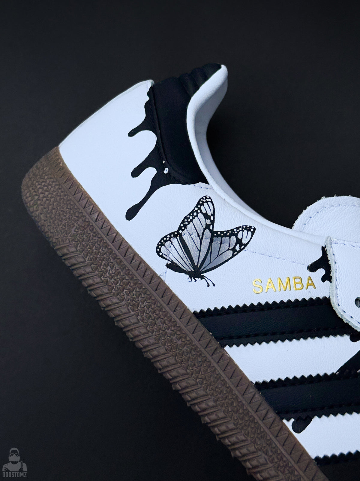Close-up of custom Adidas Samba sneaker featuring butterfly artwork, black drip design and gold SAMBA lettering