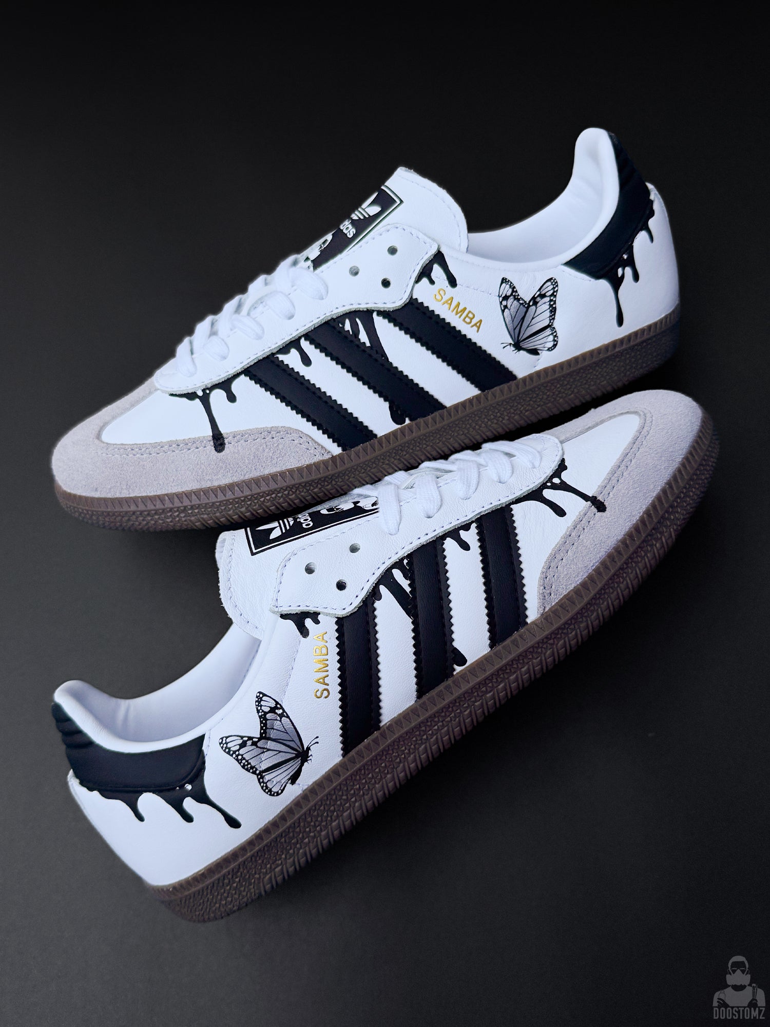 Custom Adidas Samba sneakers arranged diagonally, featuring black drips, butterfly artwork and gold SAMBA lettering