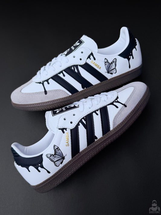 Custom Adidas Samba sneakers arranged diagonally, featuring black drips, butterfly artwork and gold SAMBA lettering